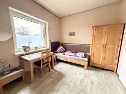 Schönes Schlafzimmer mit Einzelbett, Holzschrank und Tisch mit Stuhl in der Pension Bed and Breakfast.