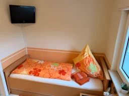 Bezugsbereites Einzelbett mit Handtüchern und Wand-TV in der Pension - Gästehaus Legden.