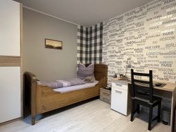 Gemütliches Zimmer in der Pension mit einem Bett, Stuhl, Schreibtisch und kariertem Wanddesign.