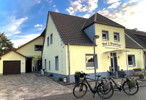Die gelbe Außenansicht der Pension in Legden mit zwei davor geparkten Fahrrädern unter blauem Himmel.