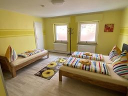 Helles Zimmer mit zwei Betten, gelben Wänden und bunten Kissen in der Pension.