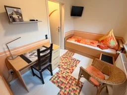 Helles Einzelzimmer mit funktionalem Schreibtisch und Sessel in der Pension - Gästehaus Legden.