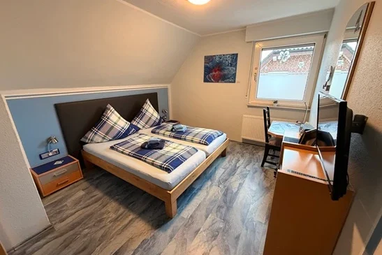 doppelzimmer-pension-legden-nahe-Stadtlohn Gemütlich eingerichtetes Zimmer mit bezogenem Doppelbett, Schreibtisch, TV und blauem Kleiderschrank nahe Stadtlohn.