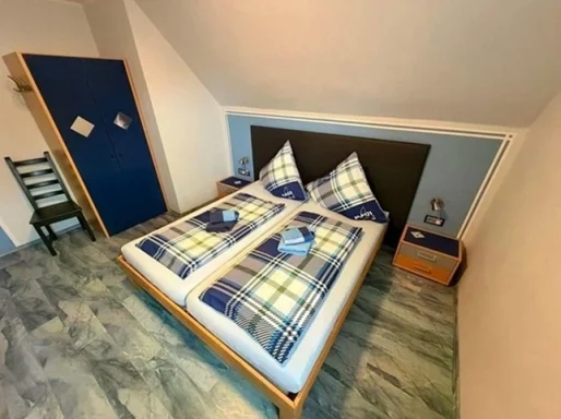 Gemütliches Doppelzimmer zum Übernachten in der Pension - Gästehaus Legden mit komfortablem Bett und blauem Kleiderschrank.