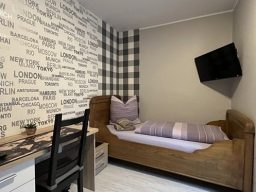 Schönes Zimmer in der Pension mit einem Einzelbett, Schreibtisch und Fernseher an der Wand.