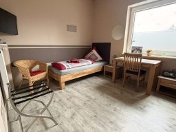 Ein einfaches Schlafzimmer mit einem Bett, TV, Stuhl und einem Tisch in der Pension Bed and Breakfast Legden.